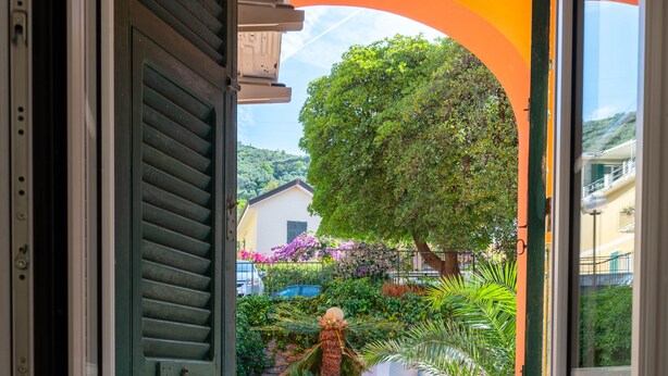 Un balcón con mobiliario de mimbre, una cesta de mimbre y vistas a un jardín exuberante.