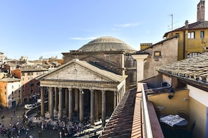 A historical building with classical architecture, including columns and a dome, surrounded by a bustling square with people and other buildings. - Pantheon View from Terrace Apartment (Rome)