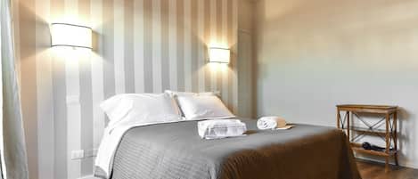 A neatly made bed with a grey quilt, two bedside lamps, and a wooden nightstand with a lamp.