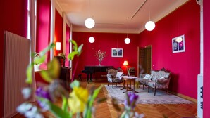 Een kamer met een rode wand, een piano, een bank en een tafel met een lamp.
