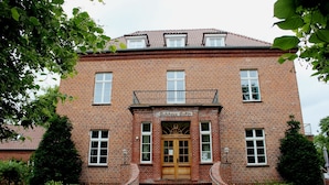 Een bakstenen gebouw met een houten voordeur, een bord boven de deur en een klein balkon.