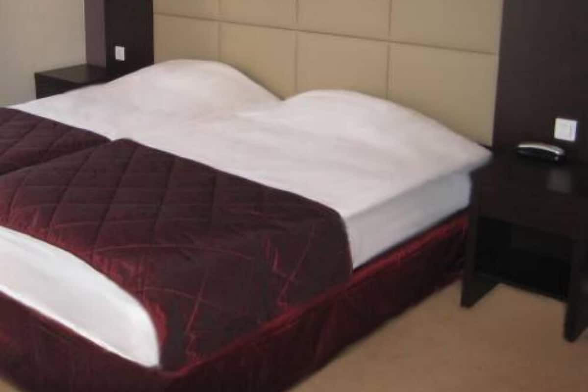 Quarto de hotel com uma cama grande, duas mesas de cabeceira e luminárias fixadas na parede.