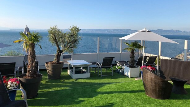 A terrace with a view of the sea, featuring outdoor furniture, potted plants, and a white umbrella. - Savoy Hôtel Evian (Evian-les-Bains)