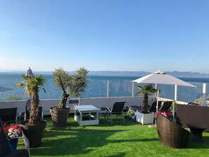 A terrace with a view of the sea, featuring outdoor furniture, potted plants, and a white umbrella. - Savoy Hôtel Evian (Evian-les-Bains)