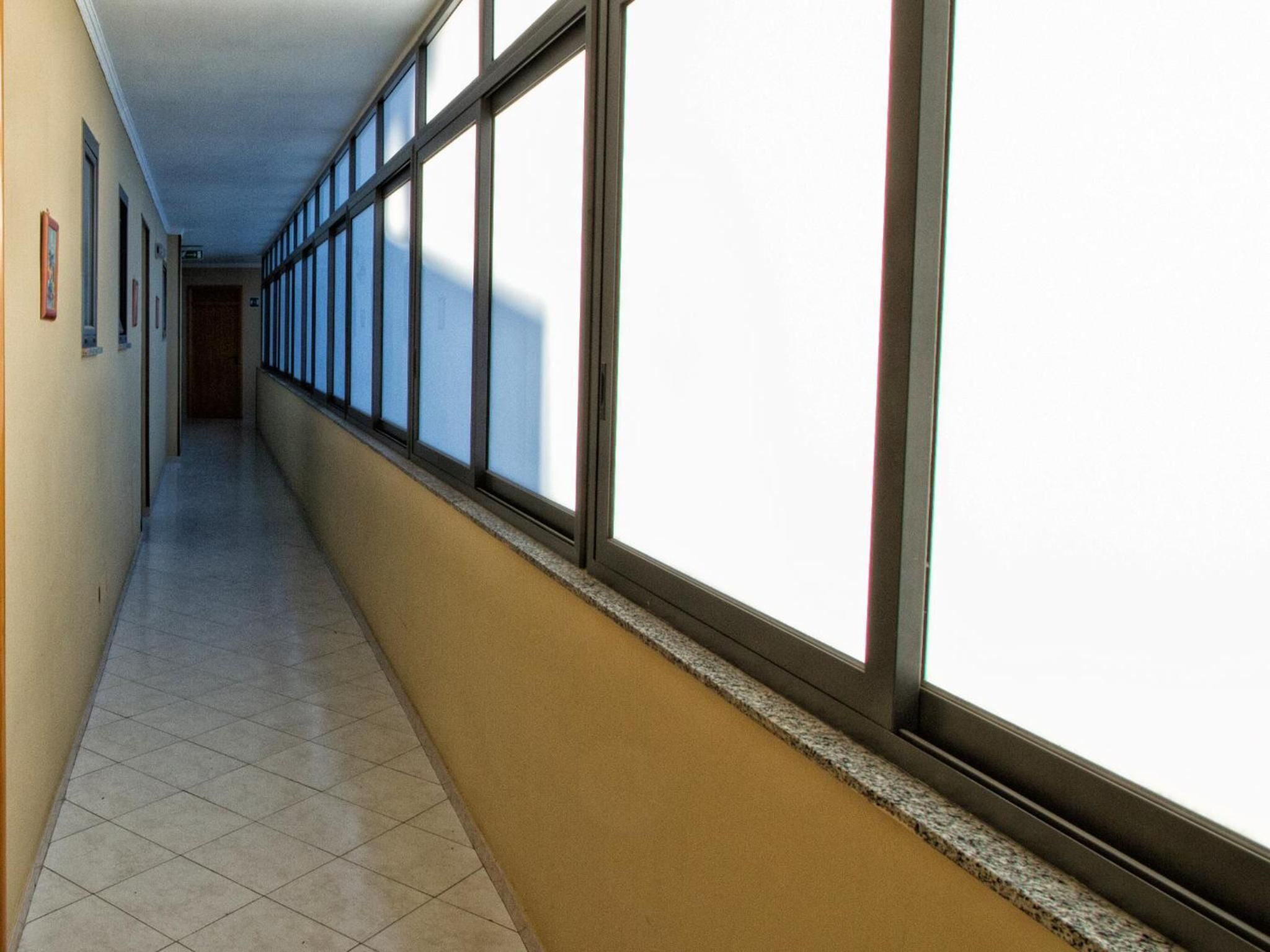A long, narrow hallway with large windows on one side and a tiled floor.