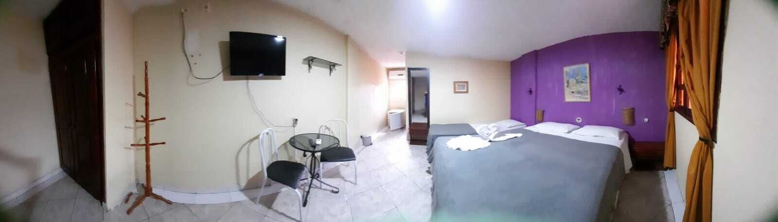 A hotel room with a bed, a TV, a small table with chairs, and a coat rack.