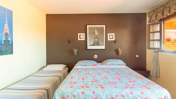 Habitación de hotel con dos camas individuales, una cama grande con cubrecama floral, un cuadro con la Estatua de la Libertad y una ventana con cortinas.