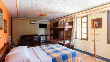 Habitación de hotel con cama, sofá, televisión, litera de madera y ventana con cortinas.