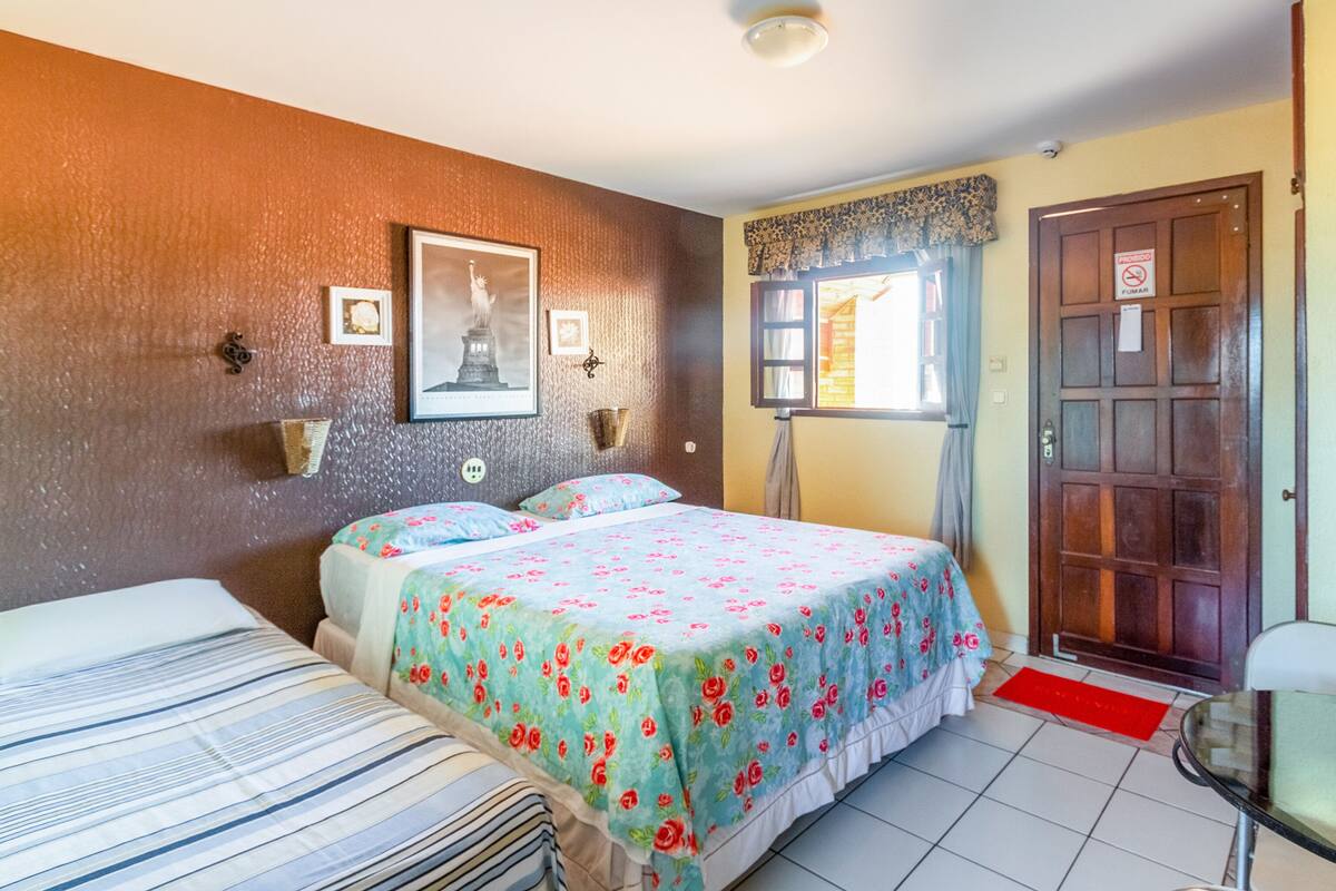 A hotel room with two beds, a framed picture of the Statue of Liberty, a window with curtains, and a door with a 'No Smoking' sign.