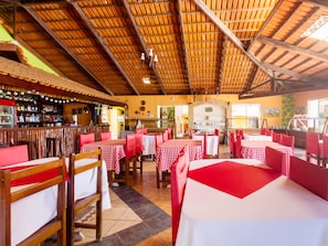 Um restaurante com toalhas de mesa xadrez vermelhas e brancas, cadeiras de madeira e teto alto de madeira.