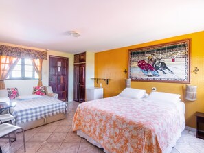 Experience a traditional hotel room with two beds, a desk, and a wall-mounted lamp, featuring a large painting of a bullfight.