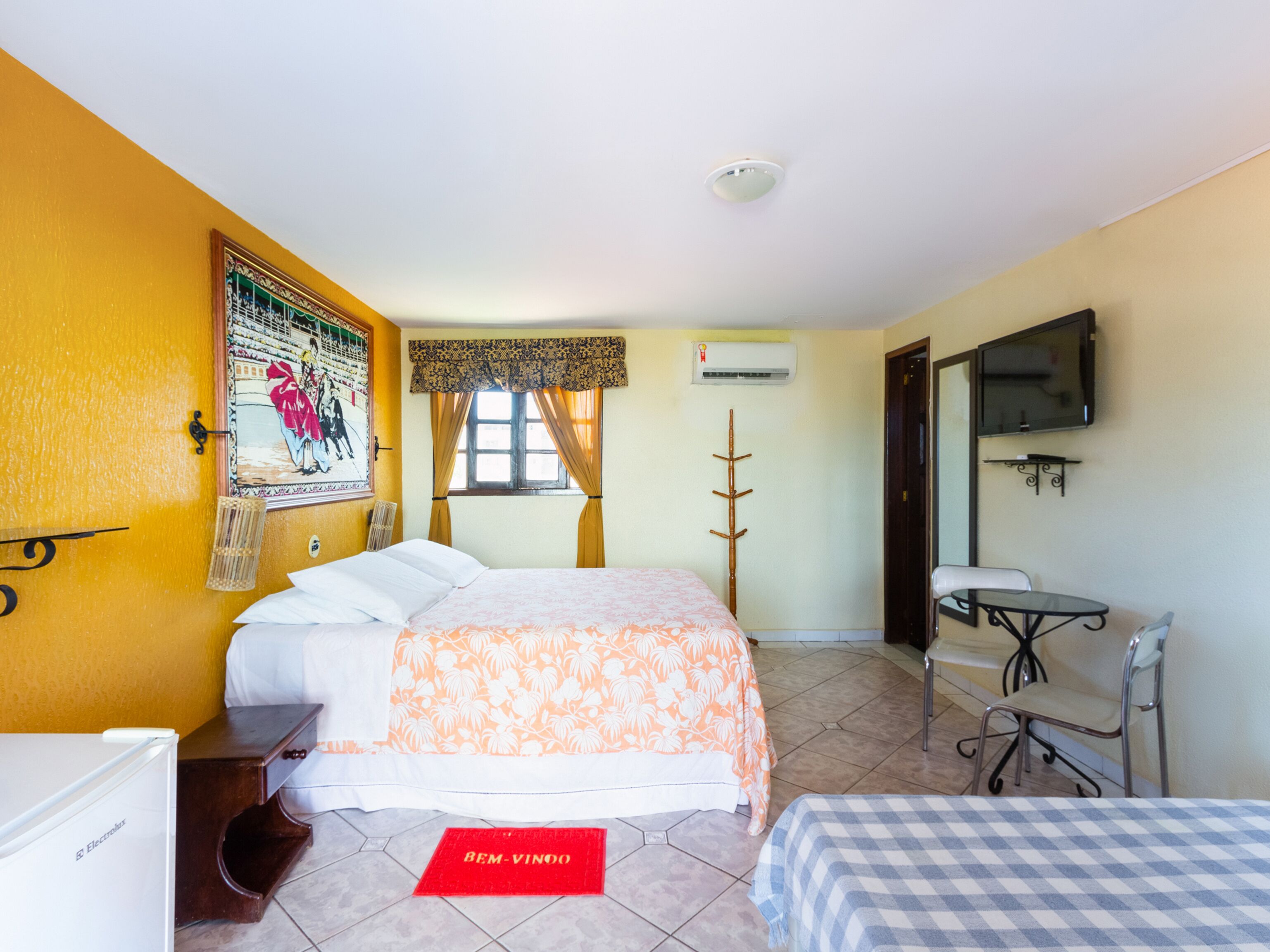 Habitación de hotel con cama, escritorio, silla, equipo de aire acondicionado y televisión en la pared.