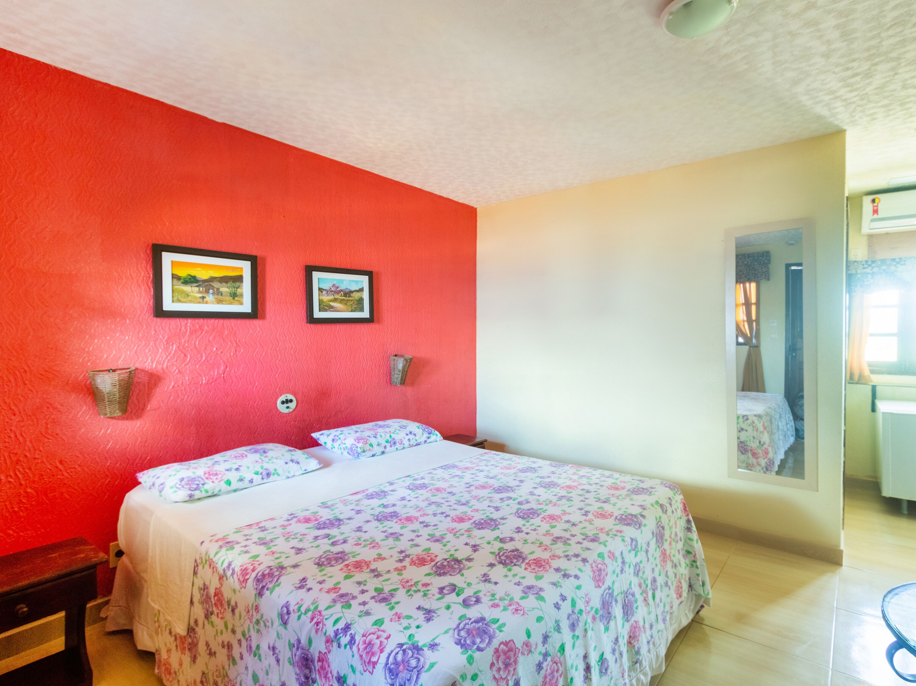Ein Schlafzimmer mit floralem Bettbezug, einer roten Akzentwand und zwei gerahmten Bildern.