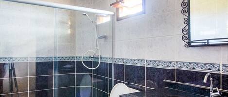 A bathroom with a glass-enclosed shower, a toilet, a sink with a marble countertop, and a mirror with a decorative frame.