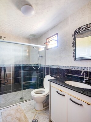 Bathroom features a glass-enclosed shower, toilet, and vanity with gold handles.