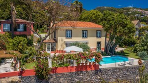 A two-story house with a swimming pool, surrounded by lush greenery and a stone wall. - Quinta D'Alegria by Our Madeira (Funchal)