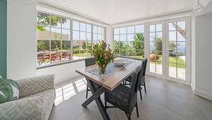 A bright, open dining area with a wooden table, black wicker chairs, and a view of a garden through large windows. - Quinta D'Alegria by Our Madeira (Funchal)