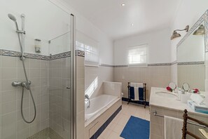 A bathroom with a glass-enclosed shower, a bathtub, a sink with a mirror, and a window. - Quinta D'Alegria by Our Madeira (Funchal)
