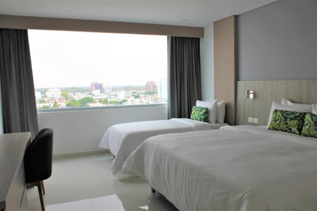 Habitación de hotel con dos camas, un escritorio y vistas a la ciudad.