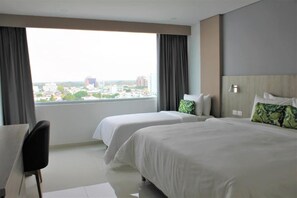 A hotel room with two beds, a desk, and a view of a cityscape. - Hotel Sexta Avenida Inn (Montería)