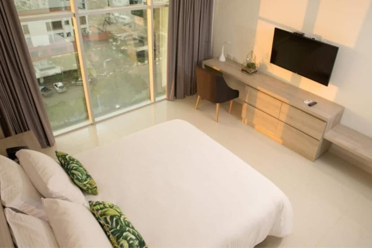 Habitación de hotel moderna con una cama grande, un escritorio, un televisor y vistas a la ciudad.