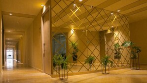 Um corredor com parede de padrão geométrico, plantas em vasos e piso espelhado.