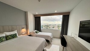 Quarto de hotel com duas camas, uma escrivaninha, televisão e uma grande janela com vista para a cidade.