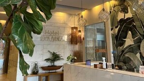 Recepção de hotel com balcão de mármore, grandes plantas verdes e design moderno no teto.