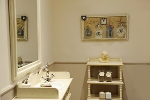 Un baño con lavamanos, espejo y decoración en la pared, incluyendo jaulas de pájaros y un adorno con forma de corazón.
