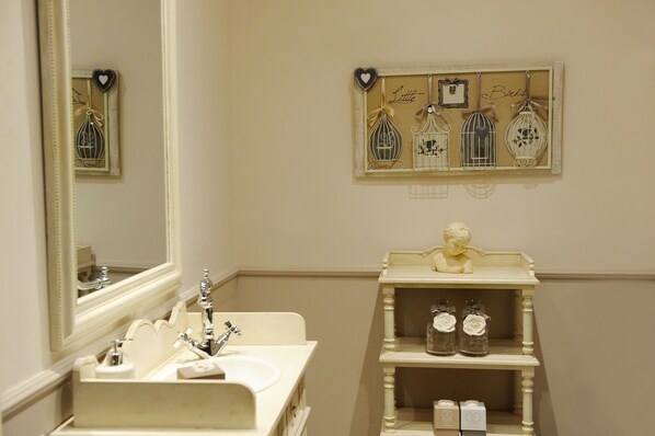 A bathroom with a sink, mirror, and decorative wall art including birdcages and a heart-shaped ornament.