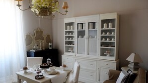 A dining area with a table set for two, a white cabinet with shelves of dishes, and a chandelier.
