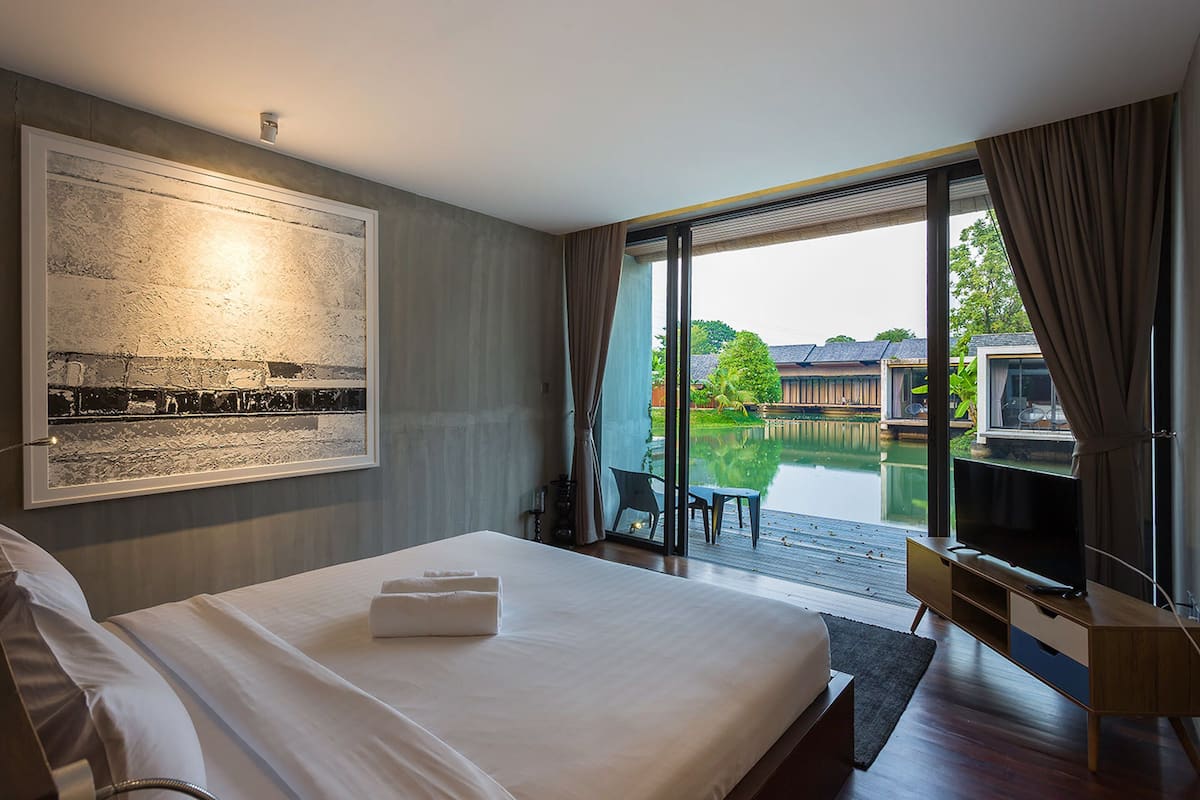 A modern hotel room with a large bed, a flat-screen TV, and a sliding glass door leading to a pool area.