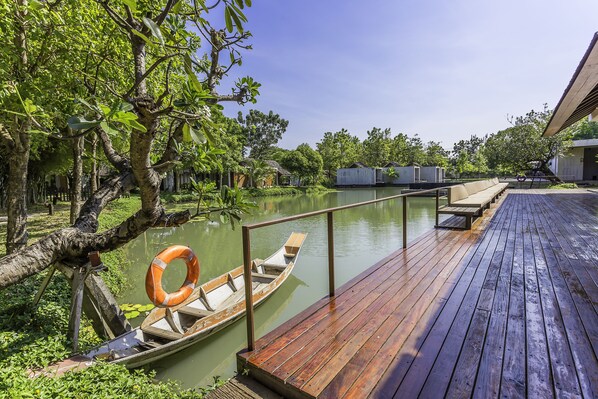 A wooden dock extending into a calm body of water, with a boat docked at the end. - Into The Forest Resort (Bang Phli)