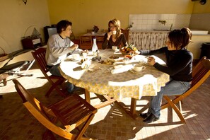 A round dining table with a yellow patterned tablecloth, surrounded by wooden chairs.
