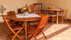 Una mesa de madera con cuatro sillas, un jarrón de flores y una cesta de fruta encima.
