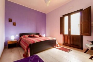 A bedroom with a bed, nightstand, and a window with wooden shutters.