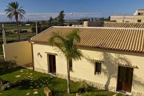 A building with a tiled roof, a stone base, and a small garden with palm trees. - B&B Solesun (Misiliscemi)