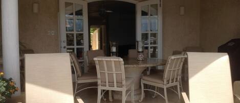 A covered patio area with wicker furniture and a glass table.