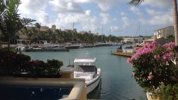A marina with boats docked, a pool area, and a view of buildings in the background. - Holiday Home at 163 Port St Charles (Speightstown)