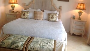 A neatly made bed with a headboard, two bedside tables with lamps, and a small nightstand. - Holiday Home at 163 Port St Charles (Speightstown)