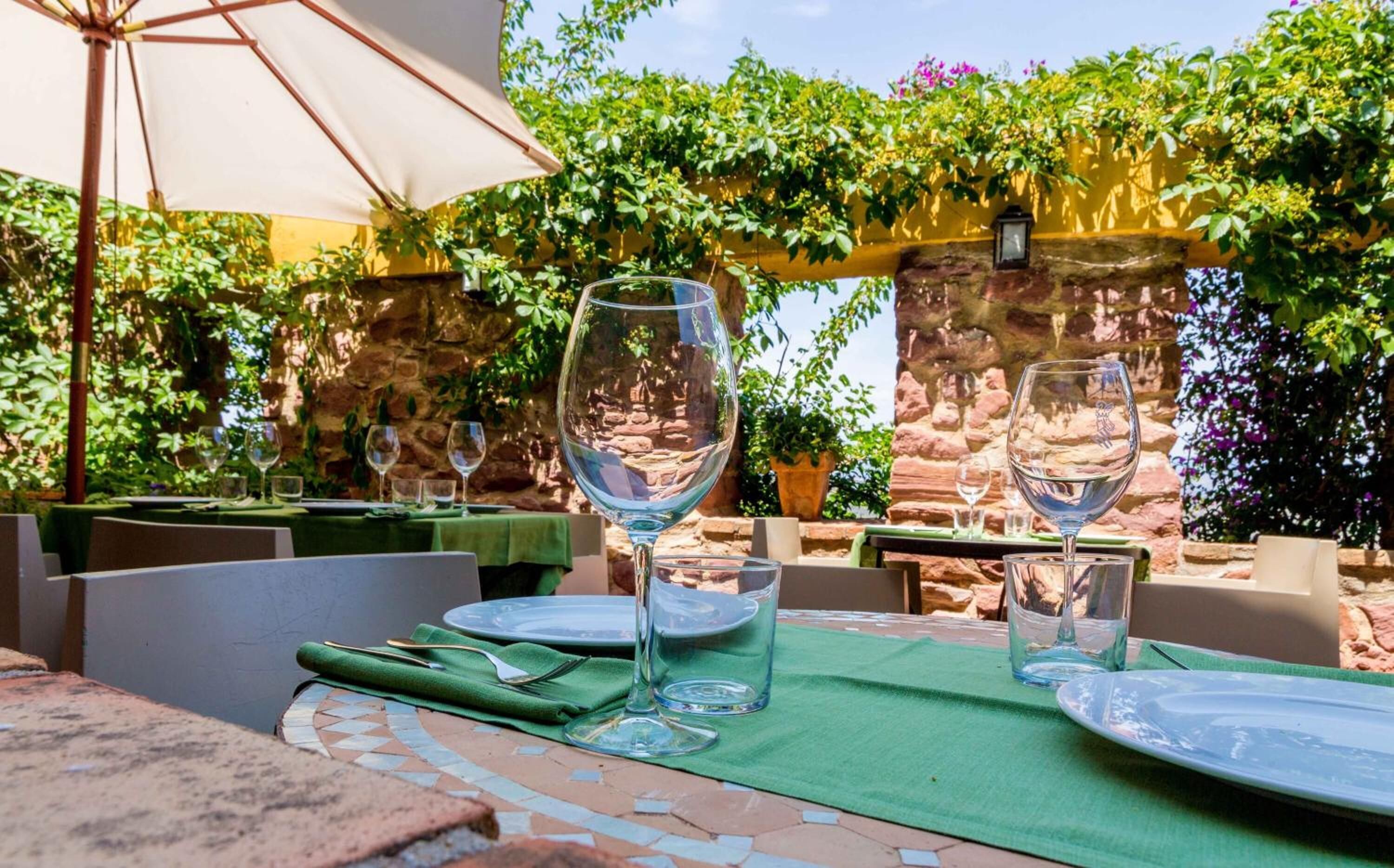 An outdoor dining area with tables set for two, each with a wine glass and a plate.