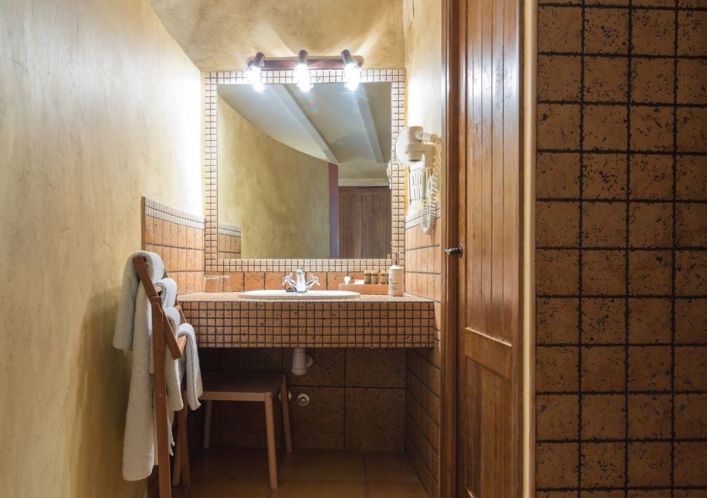 Ein kleines Badezimmer mit einem gefliesten Waschbecken, einem Spiegel mit Beleuchtung und einem Handtuchhalter.