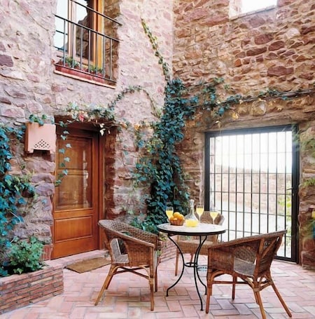 A rustic stone building with a wooden door, ivy-covered walls, and a table with chairs outside.