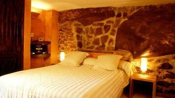 A bedroom with a stone wall, a bed with two pillows, and a nightstand with a lamp.
