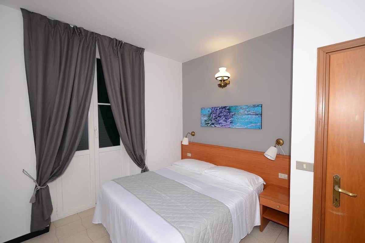 A bedroom with a bed, grey curtains, a wall-mounted light, and a painting.