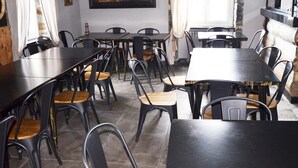 Een restaurant met meerdere tafels en stoelen, een open haard en een groot schilderij aan de muur.