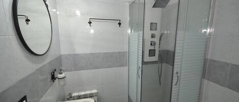 Ein modernes Badezimmer mit einer Duschkabine aus Glas, einem weißen Waschbecken und einem großen Spiegel.