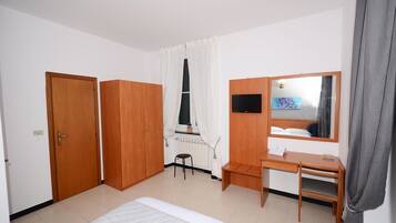 Un dormitorio con cama, escritorio, silla, armario, televisor y ventana con cortinas.