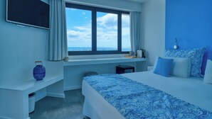 A hotel room with a large bed, a desk, a chair, a TV, and a window with a view of the sea. - Hotel Boutique La Marquesina Adults Only (La Oliva)