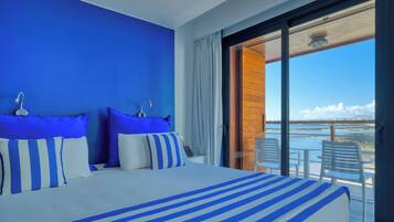 Ein Hotelzimmer mit einem großen Bett, Meerblick und einem Balkon mit Stühlen.